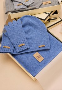 Ensemble bonnet en tricot bleu et gants avec des poignets côtelés, accompagné d'une écharpe assortie. Tous les articles sont dotés d'étiquettes en cuir et présentés dans une boîte cadeau.