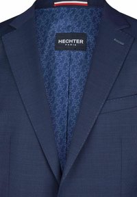 Blazer azul navy con un'esterno testurizzato e un interno a motivo. L'interno presenta il marchio HECHTER con un design geometrico ripetuto.