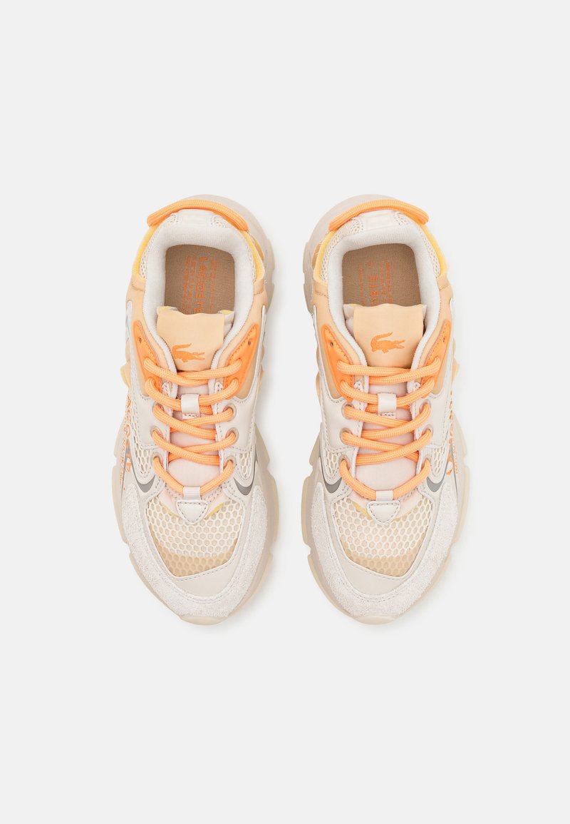 Scarpe da ginnastica beige e arancioni realizzate in materiali mesh e suede, con lacci prominenti, suola texture e un timbro del logo sulla linguetta.