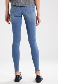 Vaaleansiniset venyvät farkut, joissa on kapea malli, keski-korkea vyötärö ja kaksi takataskua hillityllä pesulla. Yhdistetty mustiin kenkiin.