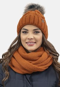 Strikket orange hue med en fluffy pom-pom og et matchende tekstureret tørklæde, begge med et kraftigt stikhætte.