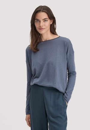 Camicia a maniche lunghe di colore azzurro chiaro, realizzata in un materiale morbido, con scollatura tonda e vestibilità comoda, abbinata a pantaloni a gamba larga di colore blu scuro.