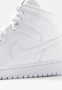 Bílé vysoké tenisky vyrobené z texturované kůže, sešívané logo Nike a kaučuková podrážka s viditelnými trakčními drážkami.