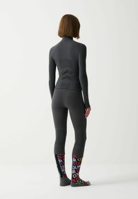 Fekete, hosszú ujjú sportfelső magas gallérral, amihez illő leggings tartozik. Színes, mintás zoknikon a "COLOR" felirat különböző árnyalatokban szerepel.