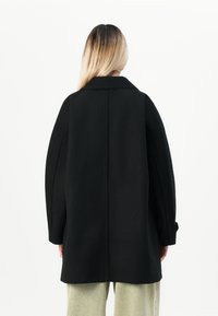 Black oversized coat with a structured collar, long sleeves, and subtle stitching details. Smooth texture, straight cut, and minimalist design.