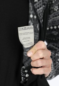 Hand holding a fleece jacket showing a care label with washing symbols and instructions in Swedish and English.