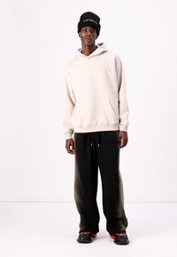 Lys beige hoodie med kengurulomme, parret med sorte sweatpants med et gradient mønster og sorte sneakers. Sort hue med logo.