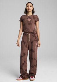 Brązowy top w stylu tie-dye z haftem kwiatowym, zestawiony z dopasowanymi, luźnymi spodniami z podobnym wzorem i delikatnymi akcentami na sznurku.