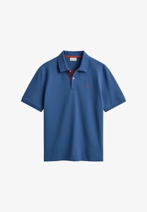 Kék rövid ujjú galléros póló belül piros patenttal, fehér gombokkal és kis piros logóval a bal mellrészen, fehér háttéren kiterítve.