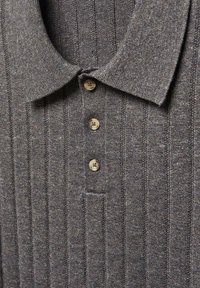 Polo gris à côtes avec col, comportant quatre boutons beiges et une poche poitrine. Tissu texturé avec des rayures verticales.