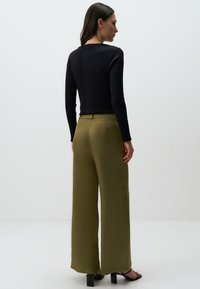 Czarny, prążkowany top z długim rękawem w połączeniu z oliwkowymi spodniami o szerokich nogawkach, charakteryzującymi się gładką teksturą i dopasowanym pasem. Czarne sandały na obcasie.