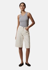 Bermudas de algodón beige con dobladillos enrollados, que presentan bolsillos frontales y un cierre de botón, combinadas con una camiseta sin mangas gris.