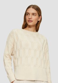Cremfarbener gestrickter Pullover mit einem sechseckigen Muster, gerippten Bündchen und Saum. Ausgestattet mit einem runden Halsausschnitt und lockerer Passform.
