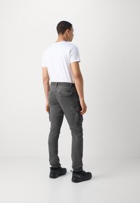 Gray cargo pants with side pockets, slim fit, and a structured waistband. Worn with a plain white t-shirt and black rugged shoes.