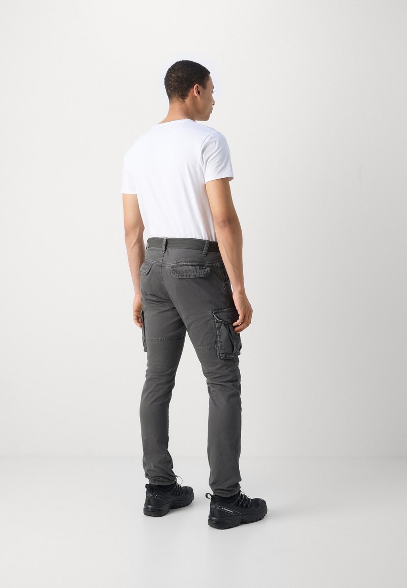 Pantalones cargo grises con bolsillos laterales, ajuste slim, y una cinturilla estructurada. Combinados con una camiseta blanca básica y zapatos negros resistentes.