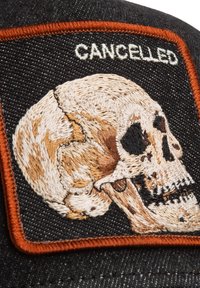 Broderet mærkat på sort stof med en detaljeret kranie og ordet "CANCELLED" i hvidt, afgrænset med orange.