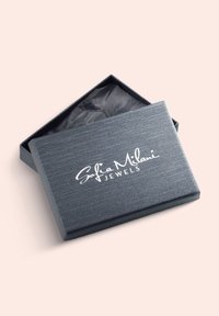 Mörkgrå smyckeslåda med texturerad yta och vitt logotyp "Sofia Milani JEWELS." Lådan är något öppen och avslöjar svart silkepapper inuti.