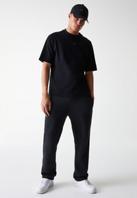 Black cotton t-shirt with a round neckline and short sleeves, paired with black tapered sweatpants and white sneakers. Black cap included.