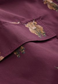 Gros plan d'un tissu bordeaux avec des bovins longhorn marron imprimés et des coutures visibles sur une section pliée.