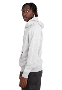 Sudadera gris de felpa con capucha con cordón, bolsillo frontal tipo canguro y puños y dobladillo acanalados, llevada con pantalones cargo oscuros.
