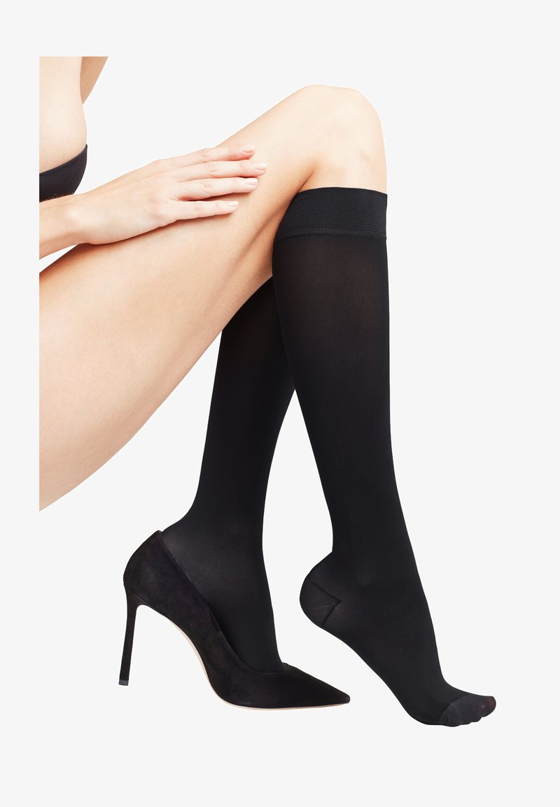 Zwarte, dijhoge stockings van doorschijnend materiaal, met een gladde textuur en zonder zichtbare patronen, gecombineerd met een zwarte suède stilettohak.