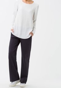Blouse blanche à manches longues avec un col rond, associée à un pantalon large à rayures verticales noires et des baskets blanches.