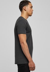 Camiseta de manga corta gris de tejido de algodón suave, diseño ajustado, cuello redondo, estilo minimalista, mostrada en un modelo de lado.