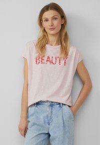 Lichtroze t-shirt met korte mouwen met het woord "SCHOONHEID" in vet, rode letters. Casual pasvorm met een zachte, gemarmerde stof.