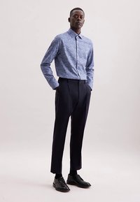 Blauw patroon overhemd met knopen en kraag, gecombineerd met zwarte op maat gemaakte broek en zwarte leren schoenen, op een neutrale achtergrond.