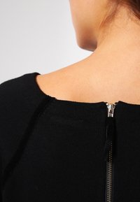 Top nero a maglia con scollo rotondo, dotato di una chiusura con zip dorata visibile nella parte posteriore. Tessuto liscio con cuciture minime.