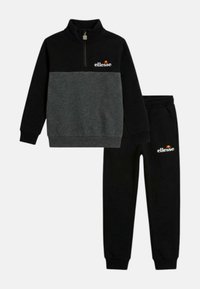 Sweat-shirt à manches longues zippé noir et gris foncé et pantalon de jogging noir avec le logo "ellesse" sur la poitrine et la cuisse gauche.