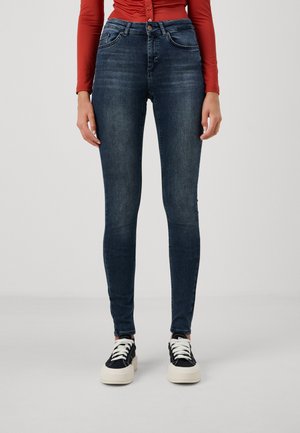 High-waisted dark blue skinny jeans made of denim with a smooth texture and subtle fading. Paired with black sneakers with white soles.