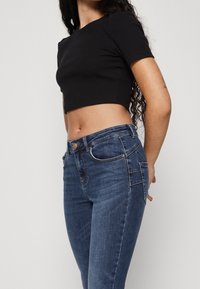 Svart cropped t-shirt som matchas med figurnära mörkblå jeans med fram- och bakt pocket, medelljus tvätt och subtila sömnadsdetaljer.