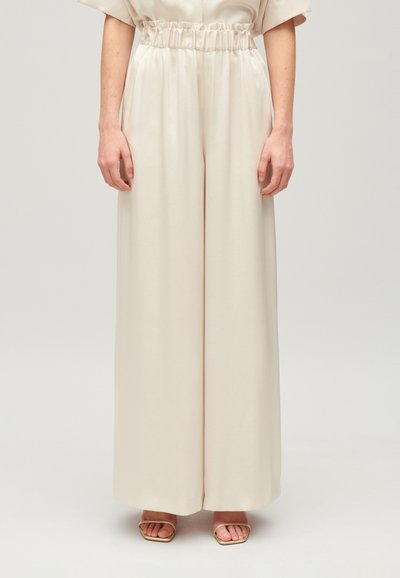 Cremefarvede vidde bukser med en blød tekstur, elastisk talje og flydende design. Styling med enkle, strappy guld sandaler.