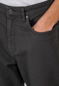 Dark gray cotton pants with a smooth texture, featuring a front pocket and a visible button with a brand logo. Tailored fit design.