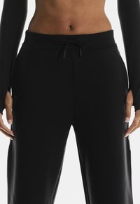 Black sweatpants with an elastic waistband, drawstring, and side pockets; smooth texture and minimal branding on the thigh.