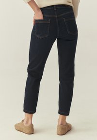 Sötétkék farmer, karcsúsított szabással, hátsó zsebekkel és felhajtott szegéllyel. Világosbarna, velúr sneakerszal párosítva.