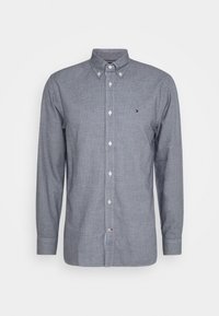 La camicia grigia a maniche lunghe ha un colletto, bottoni bianchi e un piccolo logo sul petto. È realizzata in un tessuto testurizzato.