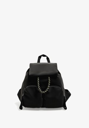 Černý látkový batoh s klopou, dekorativním žlutým úchytem, dvěma předními zipovými kapsami a polstrovanými ramenními popruhy. Elegantní, funkční design.