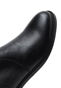 Stivaletto in pelle nera con finitura texturizzata, punta tonda e suola piatta in gomma. Le cuciture aggiungono un design sottile.