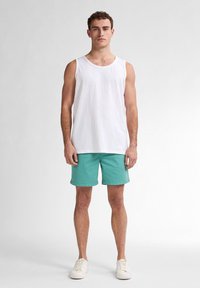 Débardeur en coton blanc associé à un short turquoise et des baskets blanches. Design simple ; le short a une coupe droite ; les matériaux semblent légers.