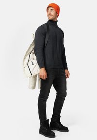 Sort turtleneck sweater, sorte jeans, sorte snørebåndsstøvler, orange striktoque og en uldjakke i hvid med lynlås, der har et flerfarvet mærke.