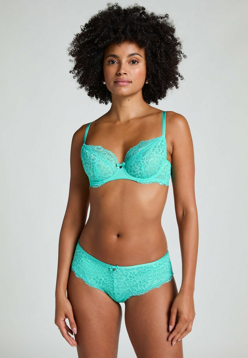 Turquoise kantenzonder beha met beugel en verstelbare bandjes, gecombineerd met bijpassende kantenen slip. Bloemenpatroon en een klein strikdetail aan de voorkant.