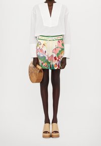 Chemise blanche à rayures avec col en V, short à motifs multicolores, sac panier en bois et sandales à plateforme beige. Design texturé et vibrant.