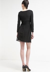 Czarna, długa sukienka z długim rękawem, dopasowaną górą i rozkloszowanym dołem, z przezroczystym wykończeniem. Nosi się z czarnymi szpilkami.