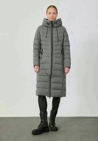Cappotto piumino grigio con cappuccio, design a righe verticali, chiusura con zip e lacci regolabili, abbinato a stivali da combattimento neri.