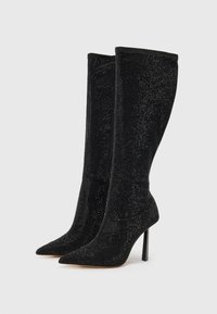 Bottines noires hauteur genou avec un bout pointu, un talon aiguille haut, et une surface texturée ornée de petites clous pour un détail supplémentaire.