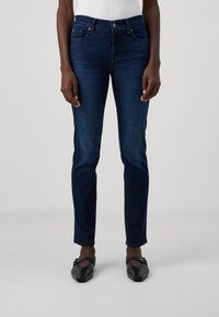 Donkerblauwe skinny jeans met een gladden denimtextuur, vijf zakken en een normale taille. Draagt met zwarte platte schoenen.