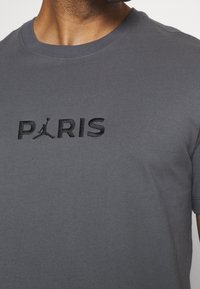 Grå bomull t-shirt med svart broderad text och logotyp "PARIS" på framsidan. Klassisk rundhals och korta ärmar.