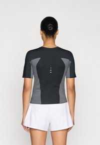 Αθλητική μπλούζα με κοντά μανίκια σε μαύρο και γκρι, με εφαρμοστή σχεδίαση, υφή στην πλάτη και αντανακλαστικές λεπτομέρειες. Το σύνολο ολοκληρώνεται με λευκά σορτς.